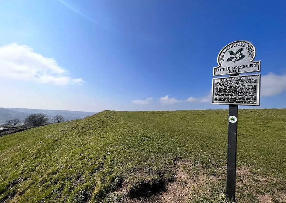 The National Trust sign for Solsbury Hill on a bright blue sky dat