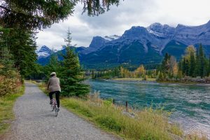 Man cycling past a river with snow capped mountains