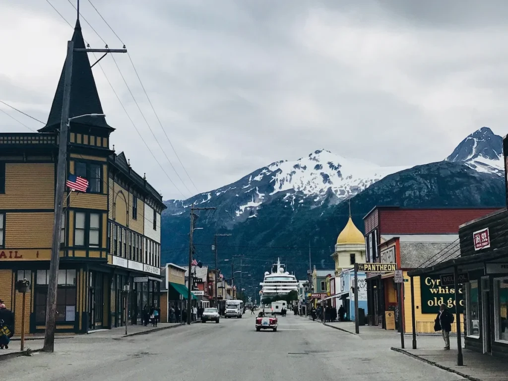 A picture looking down Skagway high street towards towering Cruise Ships in front of snow capped mountains