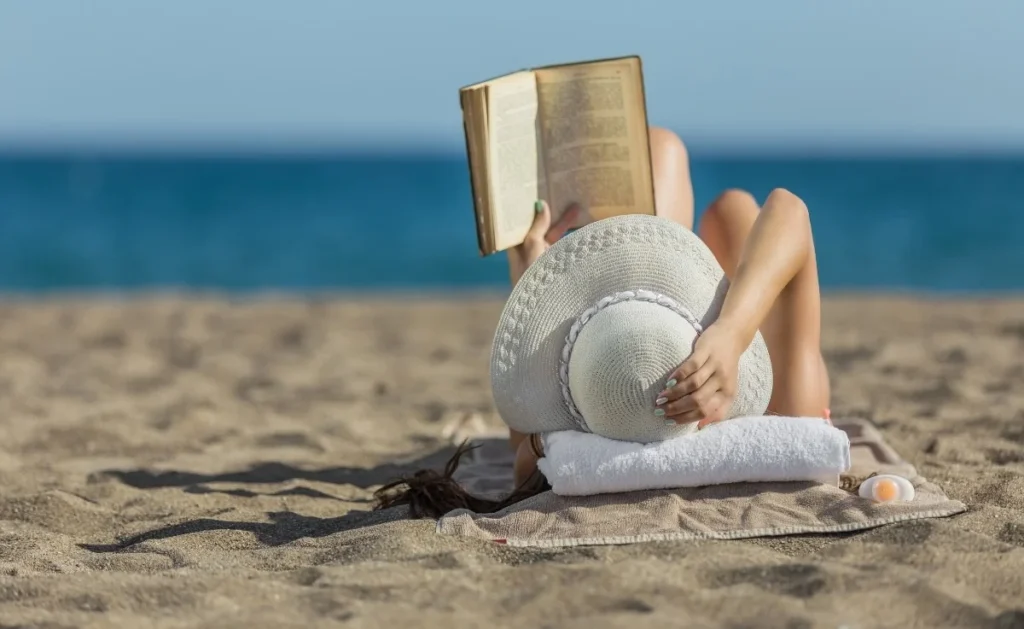 A woman lies on her back reading a book on the beach