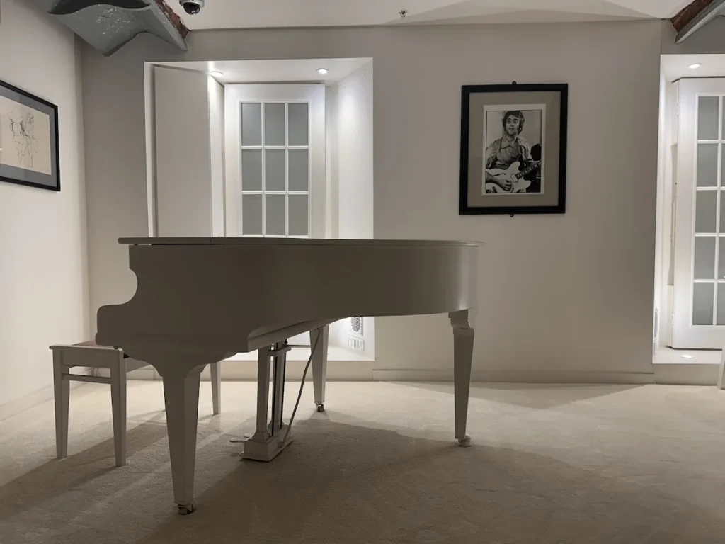 A white piano, in a white room with white carpets. Pictures of John Lennon hang on the wall. 