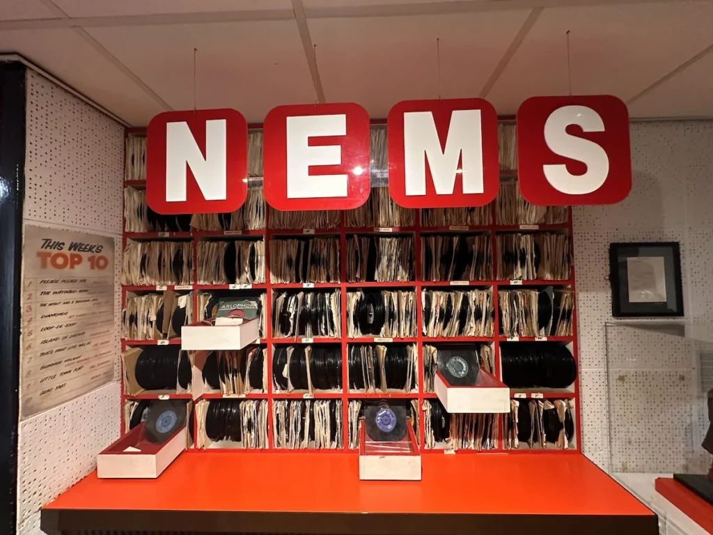 A replica of the NEMS record counter. A wall of red shelves crammed with old vinyl singles sits below four large letter signs spelling N E M S.