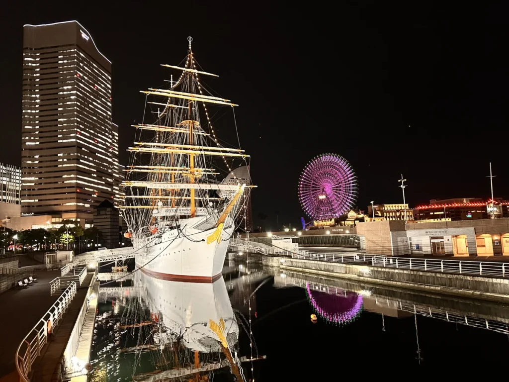 The beautiful Nippin Maru ship lit up in white contrasting the dark sky and purple big wheel in Yokohama