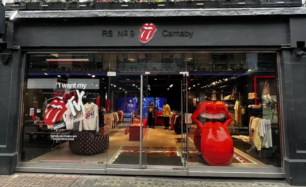 The shop front of RS9 The Rolling Stones shop in London's Carnaby Street. The dark wall hosts a bright red Tongue above the door with the windows displaying a large red tongue and other promotions