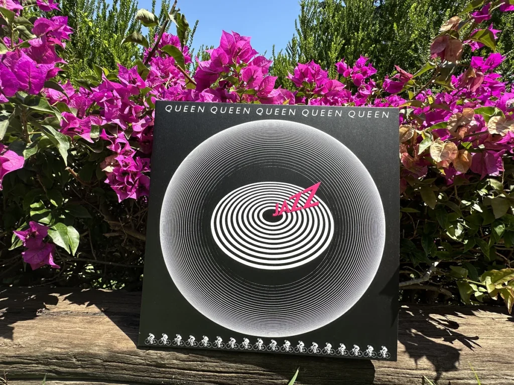 The black album cover for Queen's Jazz album stands out against the bright flowers and blue sky in the South of France