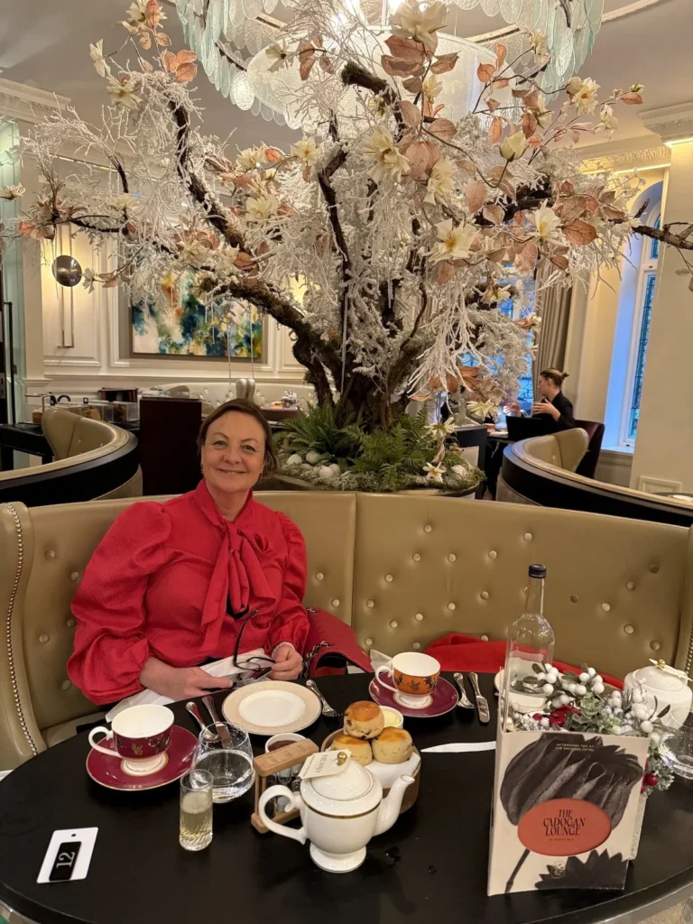 A beautiful lady in a red blouse sits beneath a decorative tree whilst a fresh set of scones and afternoon tea are placed on the table in front of her