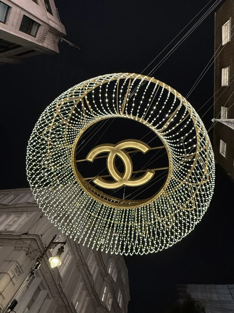 The Iconic Chanel Logo hangs surrounded by warm coloured lights above Jermyn Street set against the dark night sky