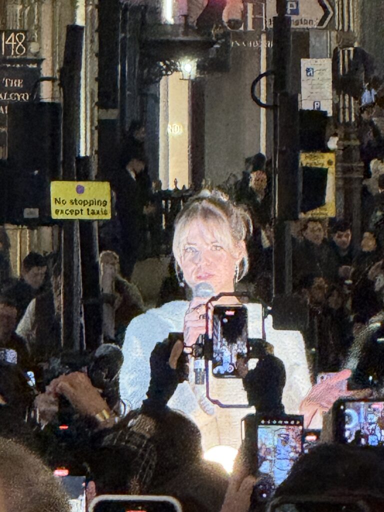 A blonde haired lady stands surrounded by camera phones as she holds a microphone to switch on the Bond Street Christmas Lights for 2024