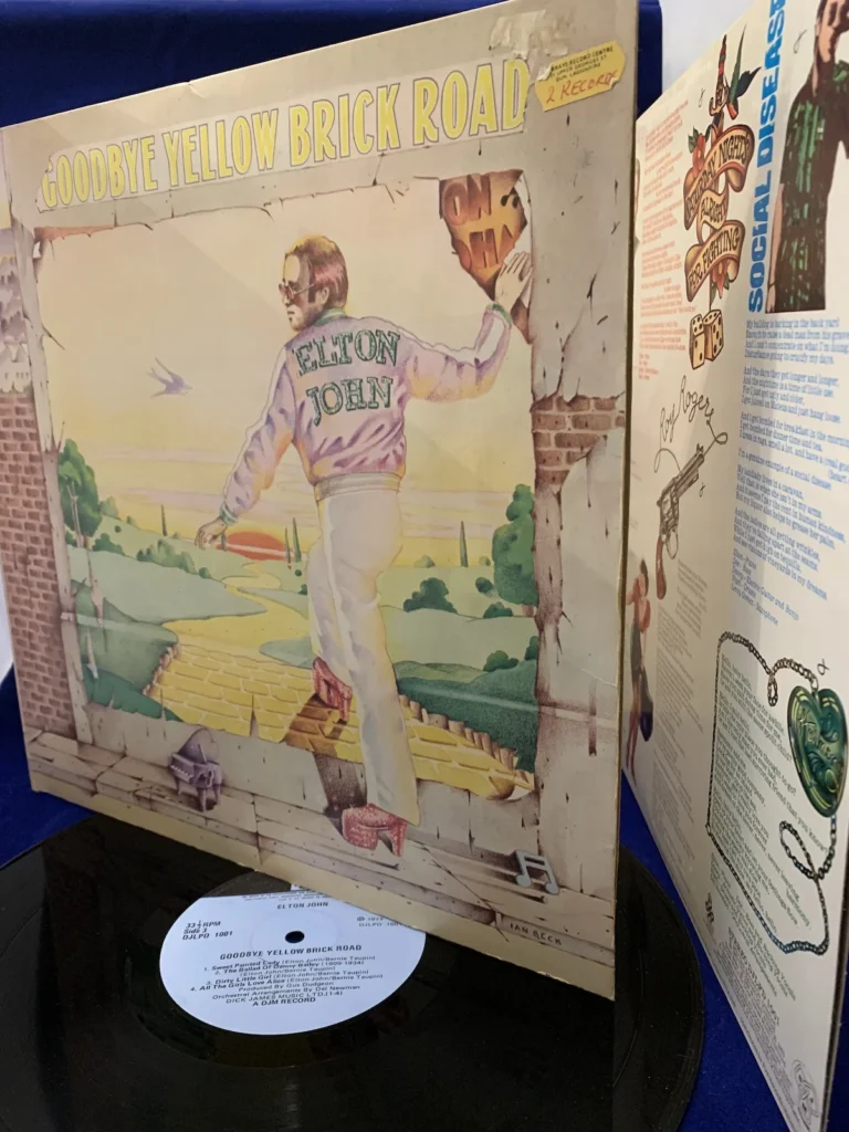 A vinyl cover for Elton John's Goodbye Yellow Brick Road propped up on top of the vinyl record