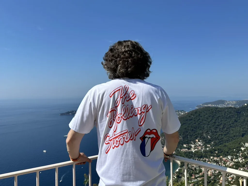 The author stands with his back to the camera, wearing a Rolling Stones T-Shirt with a French 'Tongue' logo as he gazes out to eh deep blue waters of the South of France