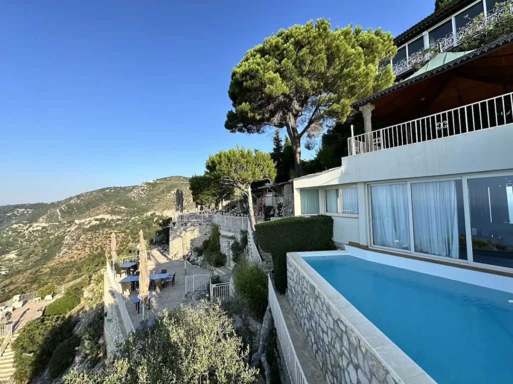 The exterior of La Chèvre D'or showing the blue swimming pool of the Nietzsche Suite, and wider terraces below 