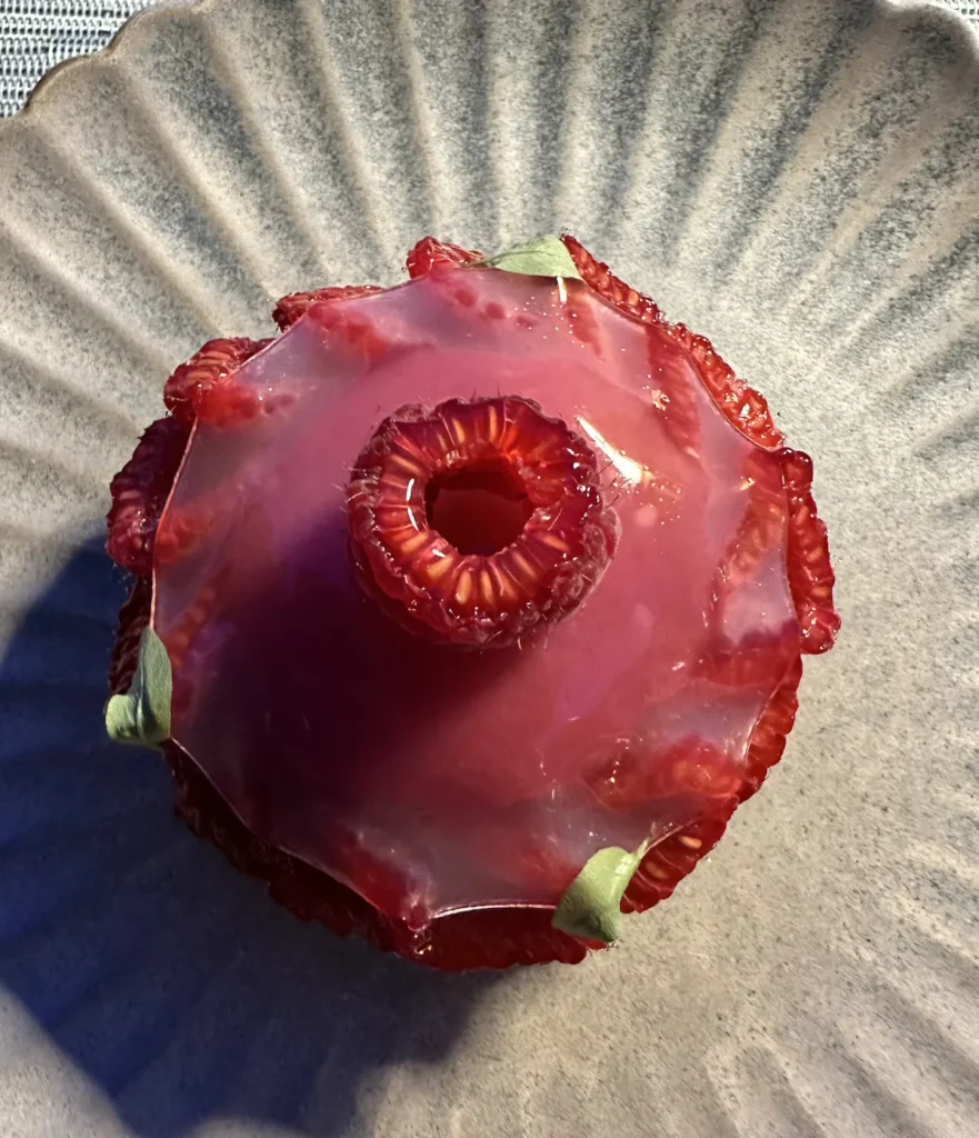 A red coloured desert tart with a small raspberry on tip