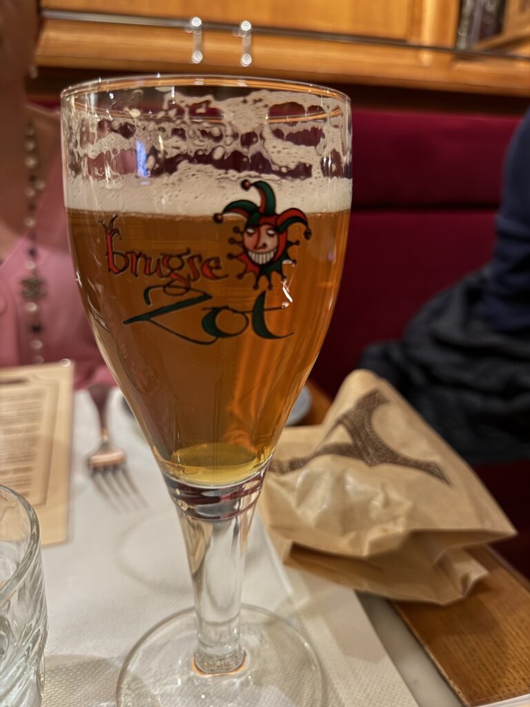 A close up of a Belgium beer glass with a red and black Jester motif for 'Brugge Zot' beer