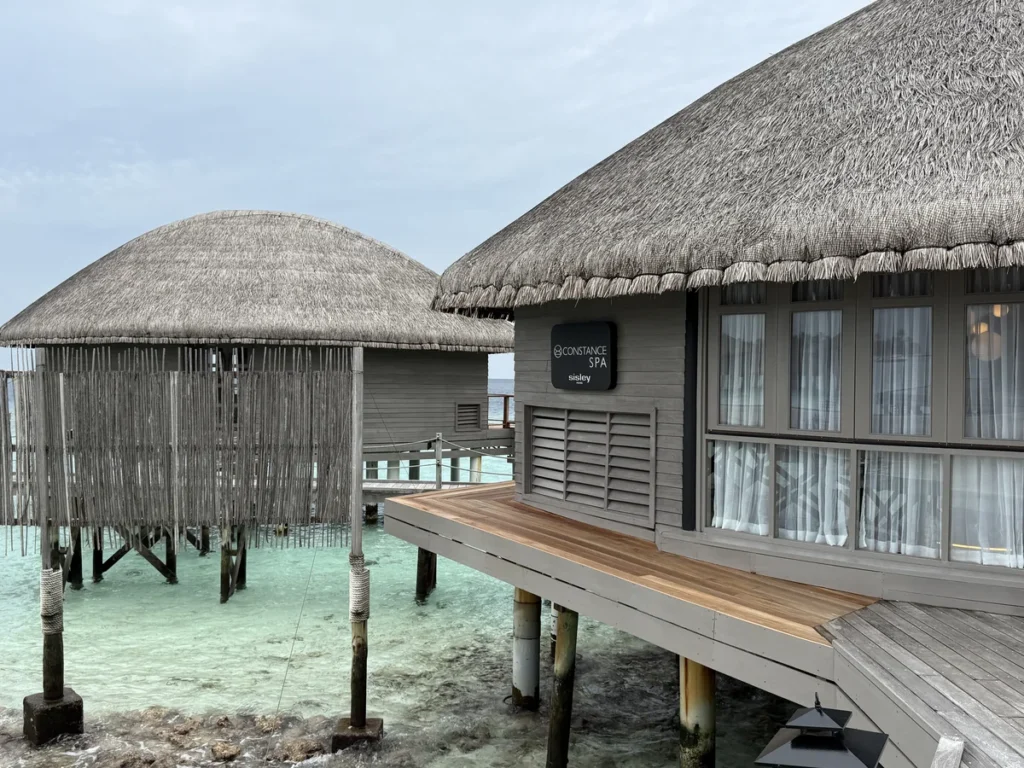 An exterior view of the Constance Spa over water treatment rooms above a turquoise sea