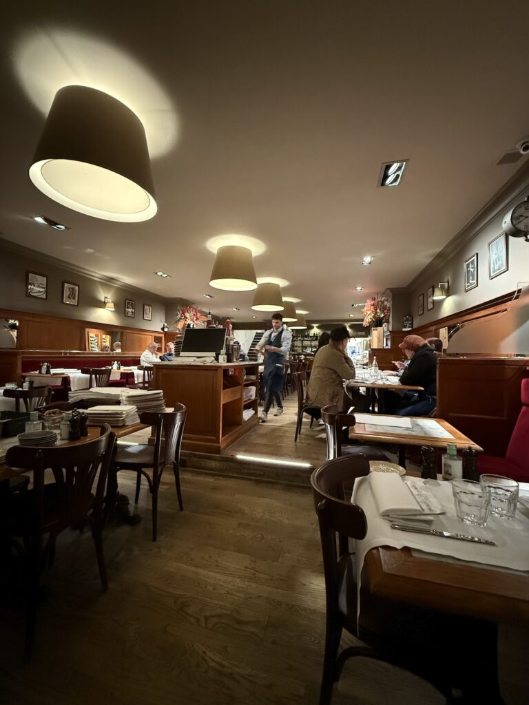 The interior decor of Brasserie Raymond with white table cloth tables, wood panelled walls and large round lights hanging from the ceiling