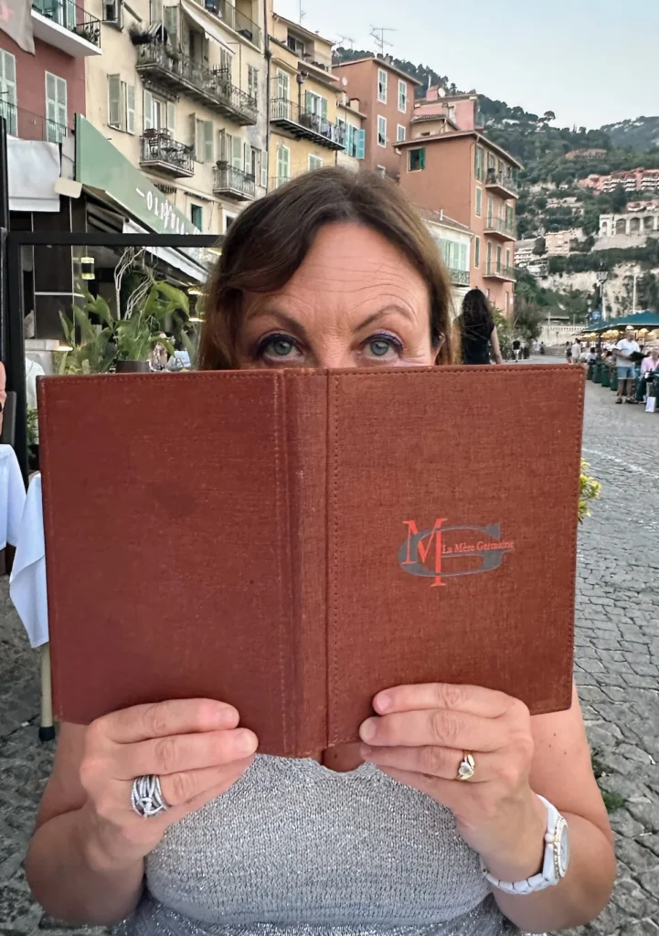 An attractive lady peaks her eyes above the menu of Mère Germain restaurant in Villefranche