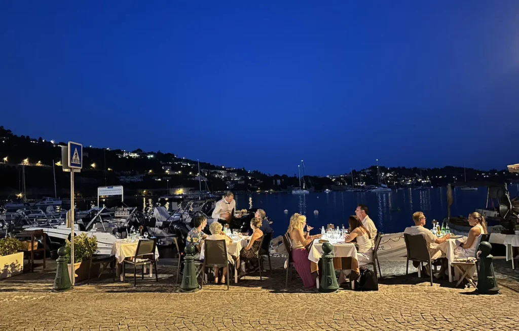 The sky is an inky blue as we look towards diners seated next to the water in Villefrance