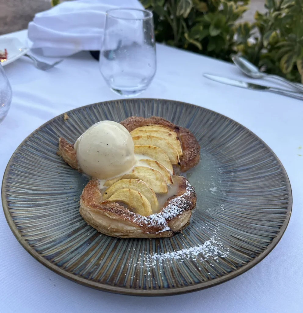 Apple tart with a dusting of sugar is topped by white vanilla ice cream on a dark ridges plate at Mère Germain restaurant in Villefranche