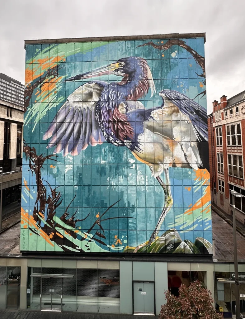 A large mural of a bird on a grey Manchester wall