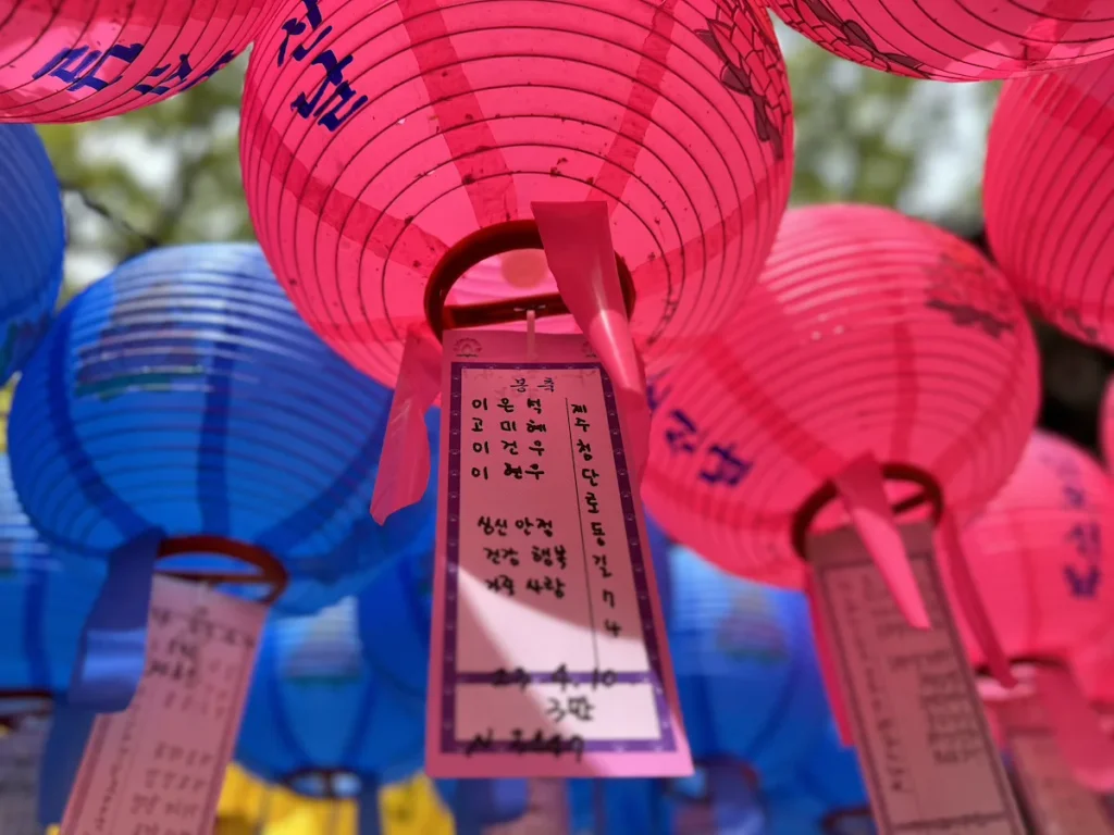 Vibrant pink and blue prayer lanterns with handwritten wishes hang in a South Korean temple