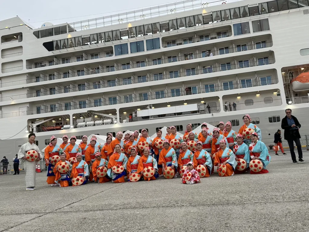 Traditional cherry dancers performing at Sakata Port with the Silver Muse cruise ship docked behind them, part of the warmest welcome on our Japan cruise.