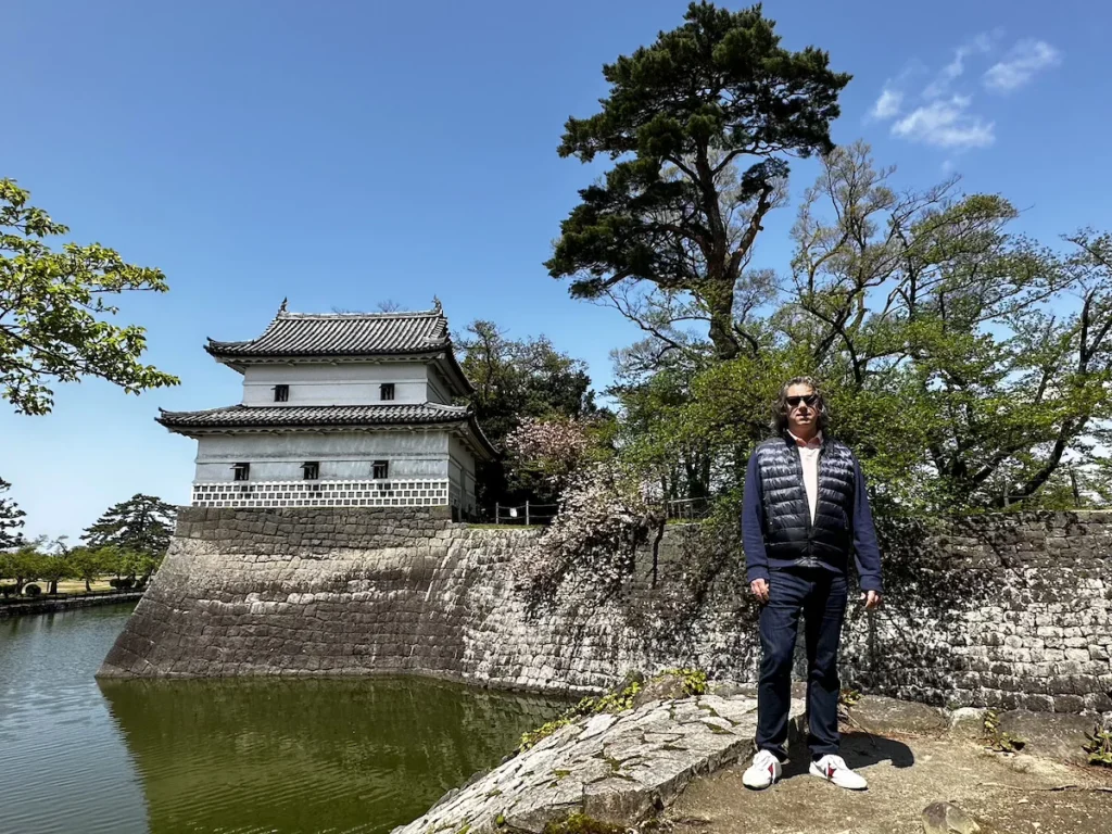 Standing by the moat of Shibata Castle, a historic Edo-period structure in Niigata, surrounded by cherry blossoms and lush greenery