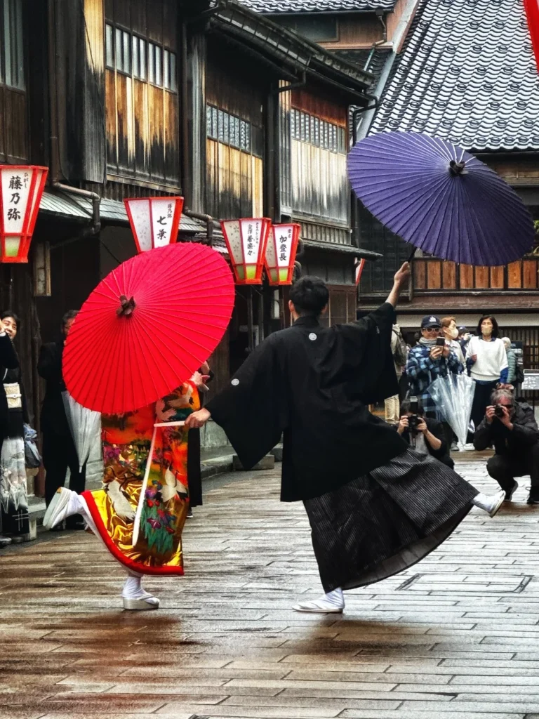 A traditional dance performance in Kanazawa’s Higashi Chaya District, featuring performers in vintage kimono and hakama, holding red and purple umbrellas.