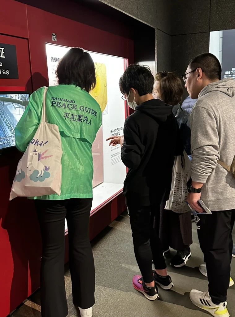 Nagasaki Atomic Bomb Museum Peace Guide guide explaining an exhibit to visitors ©Wine, Travel & Song