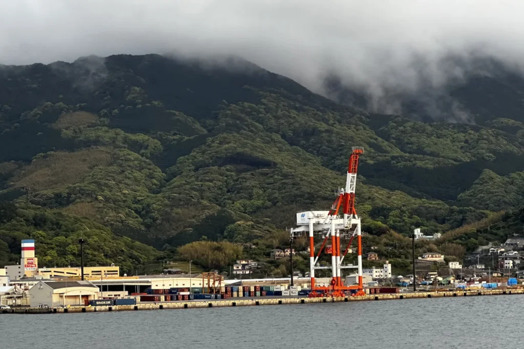 A dramatic view of the Nagasaki shipyard with towering cranes and a backdrop of misty mountains, showcasing the city’s industrial significance