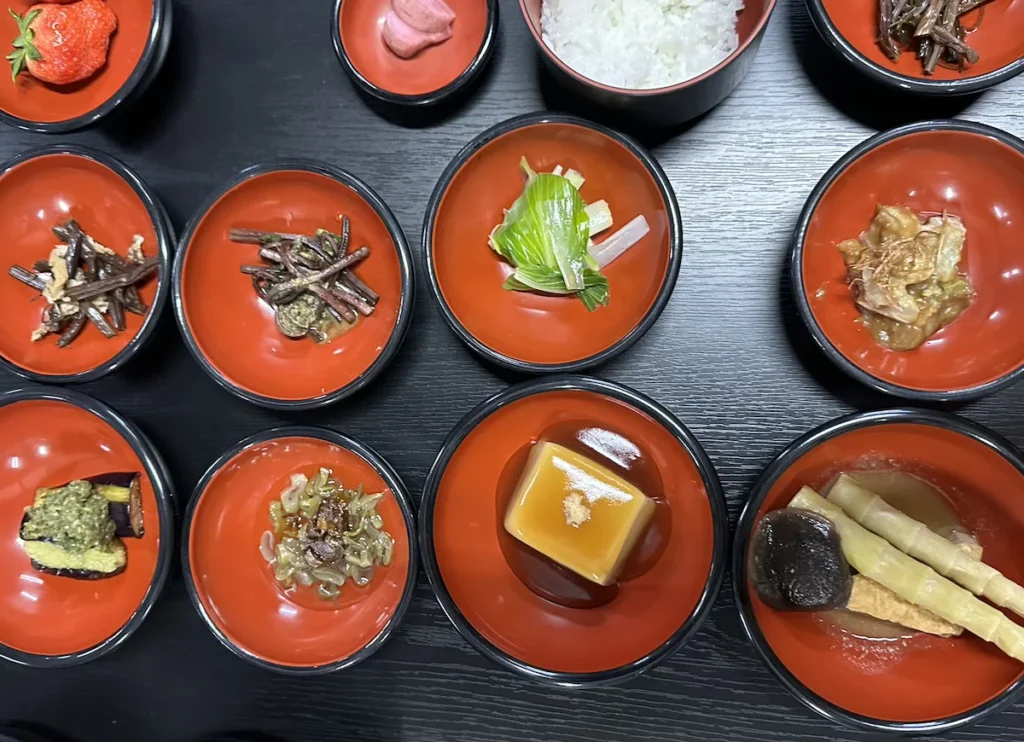 A traditional shojin ryori (Buddhist vegetarian) pilgrim’s dinner on Mount Haguro, Japan, served in lacquered red bowls. The meal includes seasonal mountain vegetables, tofu, pickles, and rice, reflecting the spiritual and culinary traditions of temple cuisine. © Wine Travel and Song.